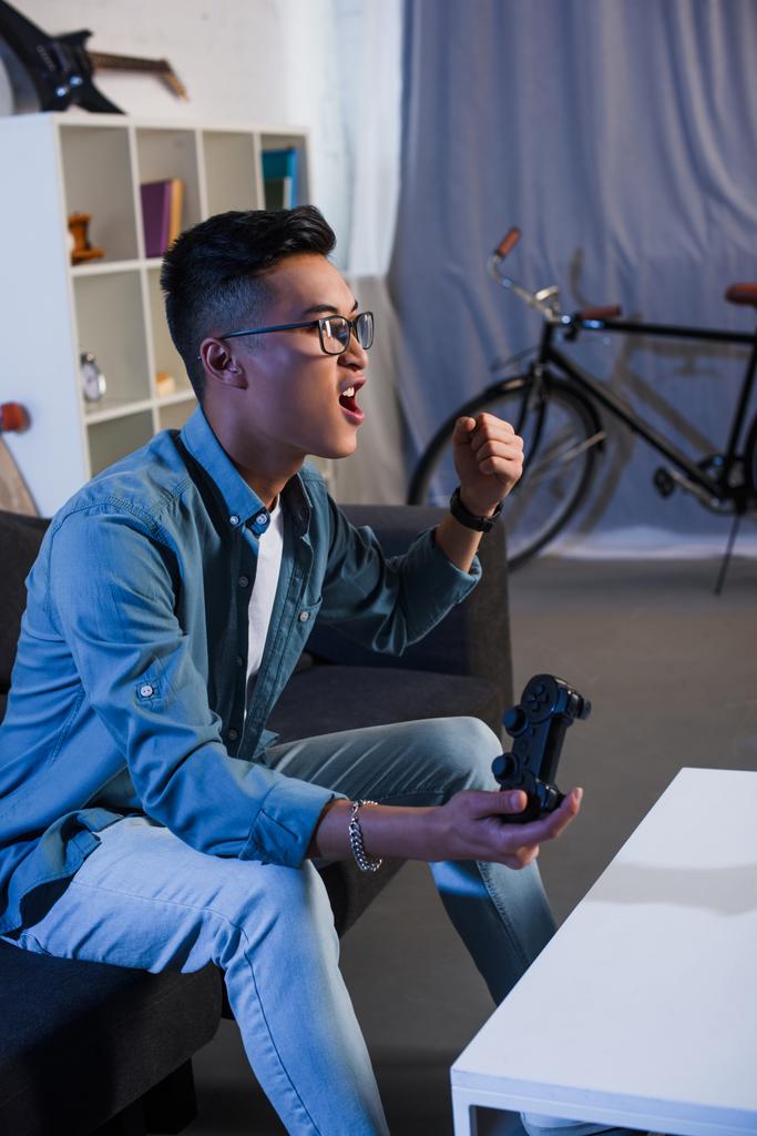 innoissaan nuori aasialainen mies pelaa videopeliä joystick ja voittaa kotona
  - Valokuva, kuva