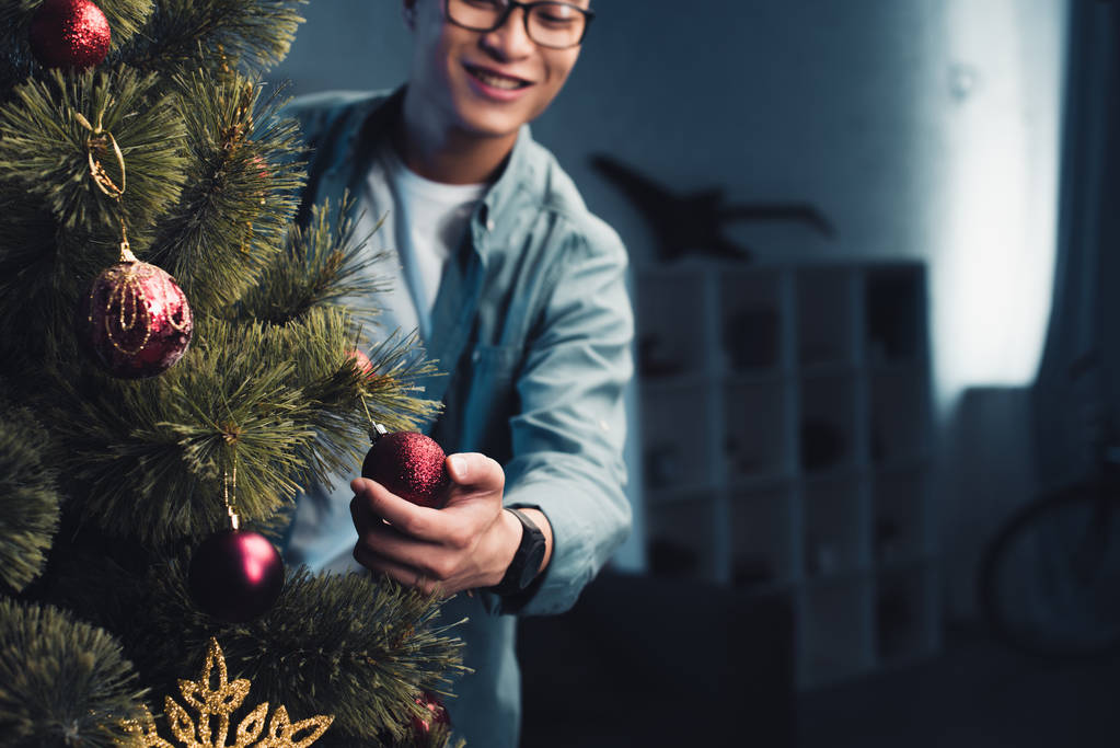 обрізаний знімок щасливого молодого азіатського чоловіка, який прикрашає ялинку вдома
 - Фото, зображення