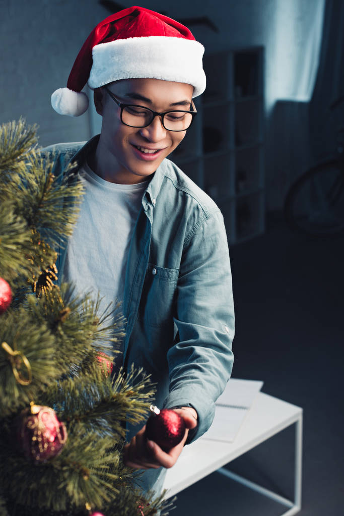 bonito sorrindo jovem asiático homem no santa hat decoração natal árvore no casa
  - Foto, Imagem