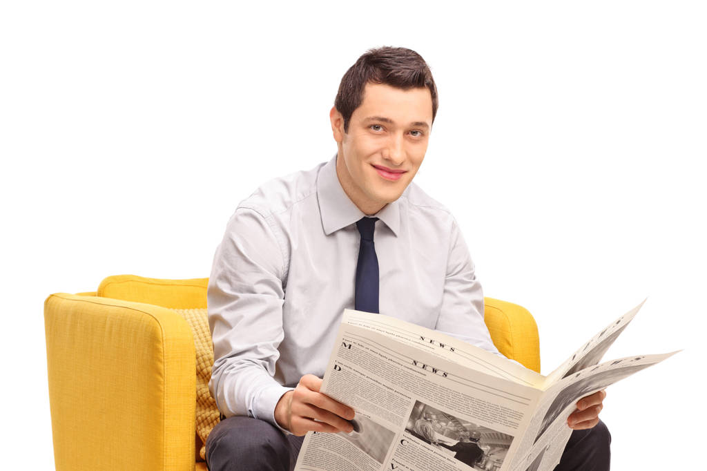 Biznesmen z gazety, siedząc w fotelu żółty na białym tle - Zdjęcie, obraz