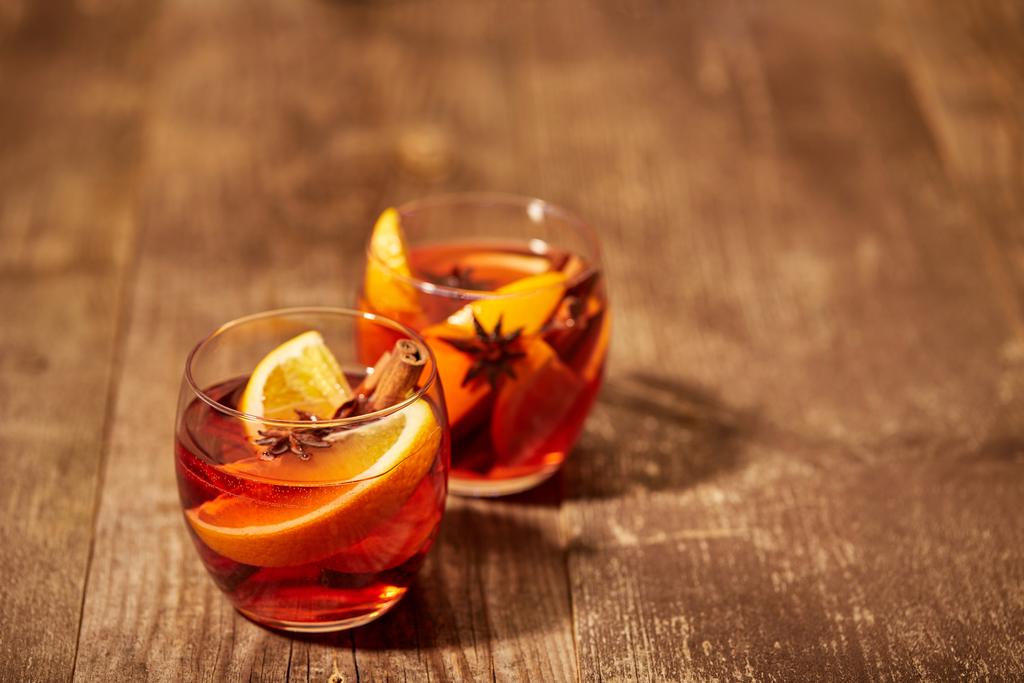 close up view of hot mulled wine drinks with spices and orange pieces on wooden tabletop - Photo, Image