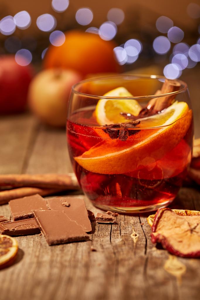 close up view of tasty mulled wine drink, chocolate and spices on wooden surface with bokeh lights on background - Photo, Image