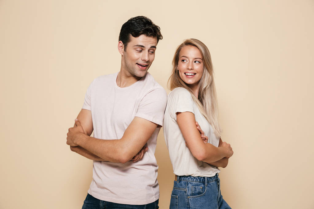 Portrait d'un jeune couple heureux debout ensemble sur fond beige, se regardant
 - Photo, image