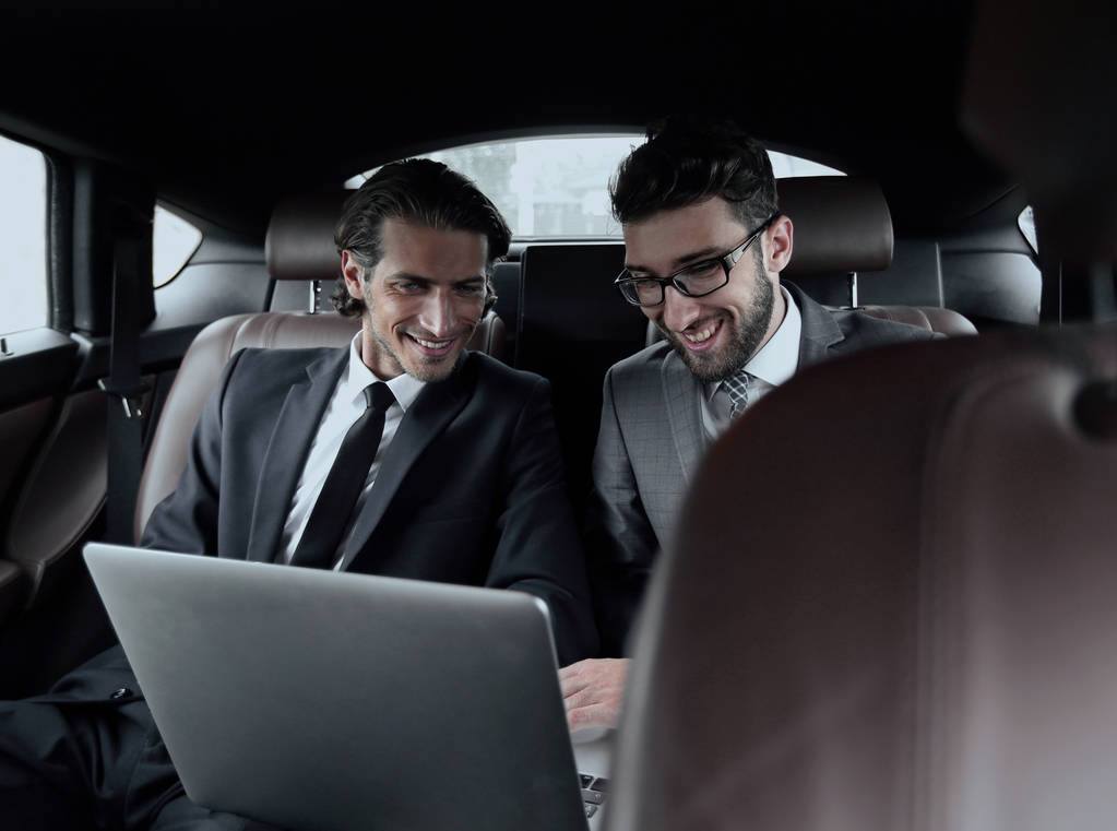 kaksi liikemiestä puhuu istuessaan autossa
 - Valokuva, kuva