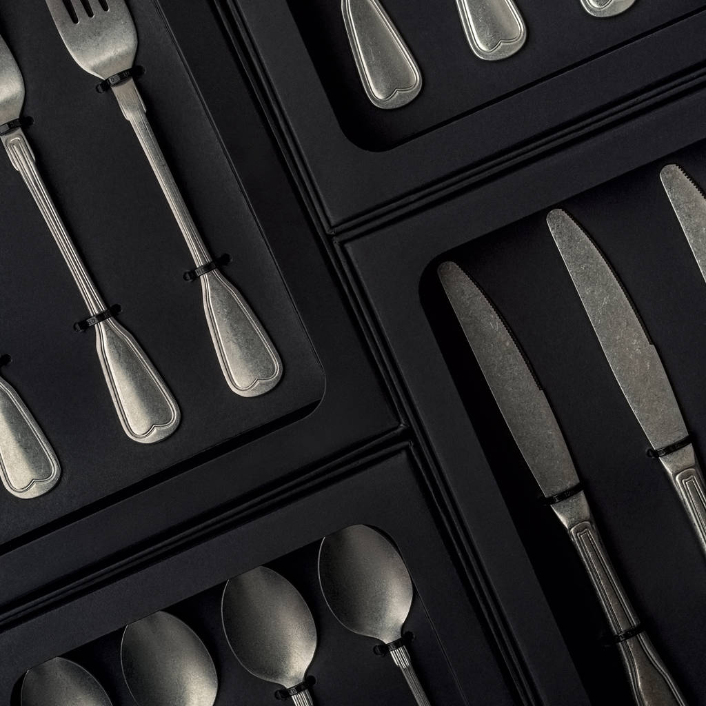Vista superior de la colección de plata de cuchillos, tenedores, cucharas, cucharadas y cucharaditas en cajas negras sobre fondo de hormigón gris
 - Foto, imagen
