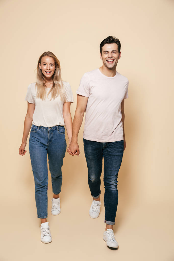 Photo of cute happy young loving couple walking isolated over beige wall background. - Photo, Image