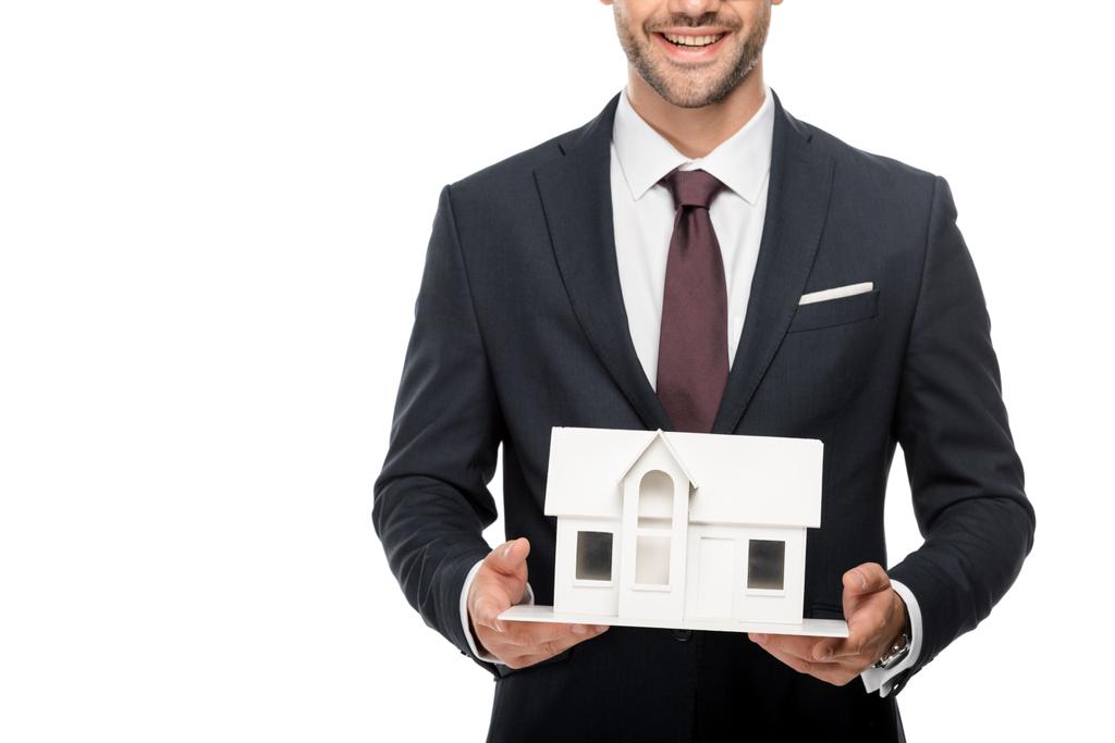 gedeeltelijke weergave van jonge mannelijke architect in formele pak toont miniatuur huis geïsoleerd op wit  - Foto, afbeelding