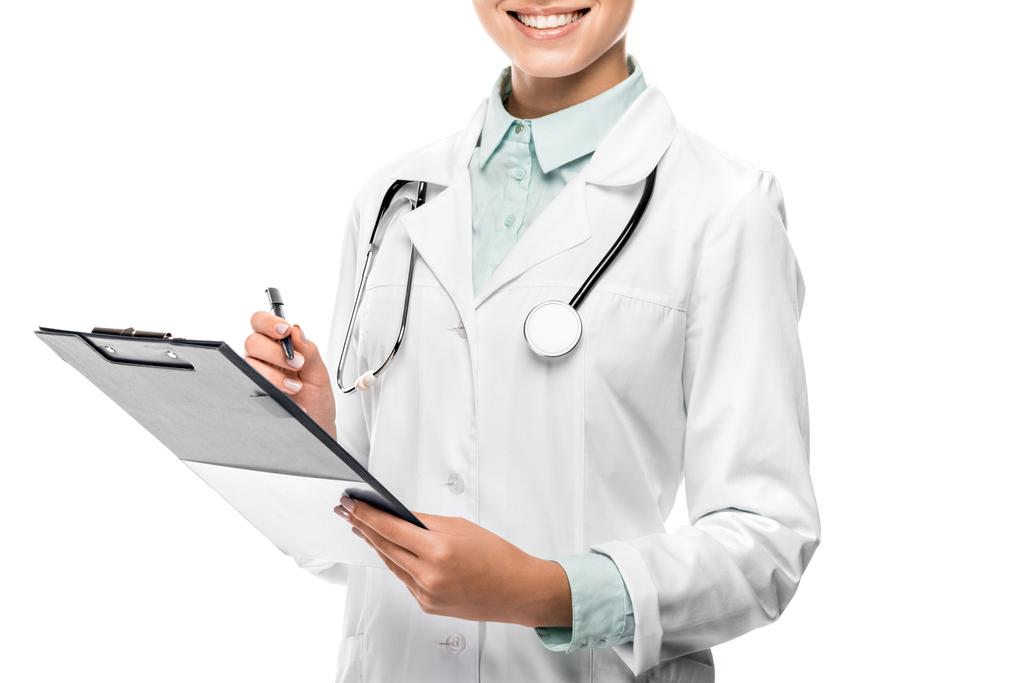 Μερική άποψη της γυναίκα γιατρό σε ιατρική παλτό γράφοντας στο Πρόχειρο που απομονώνονται σε λευκό - Φωτογραφία, εικόνα