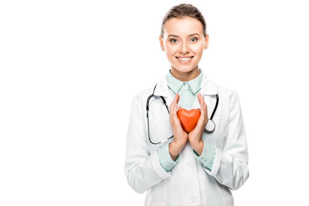 εύθυμη νεαρή γυναίκα γιατρός με στηθοσκόπιο πάνω από λαιμό που δείχνει το σύμβολο της καρδιάς εμφανίζεται απομονωθεί σε λευκό - Φωτογραφία, εικόνα
