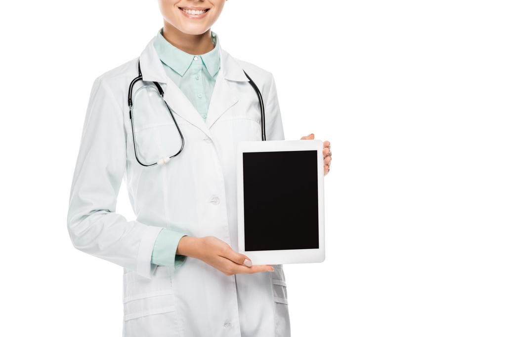 Teilansicht einer glücklichen Ärztin in medizinischem Mantel, die ein digitales Tablet mit leerem Bildschirm zeigt, isoliert auf weiß - Foto, Bild