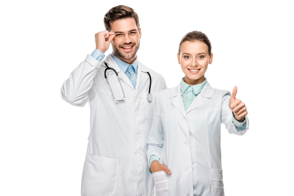 attraktive Ärztin macht Daumen hoch Geste, während ihr männlicher Kollege in der Nähe isoliert auf weiß stehen  - Foto, Bild