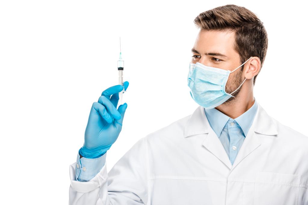 uśmiechający się młody mężczyzna lekarza w Rękawice lateksowe i maseczkę medyczną, trzymając strzykawkę na białym tle  - Zdjęcie, obraz
