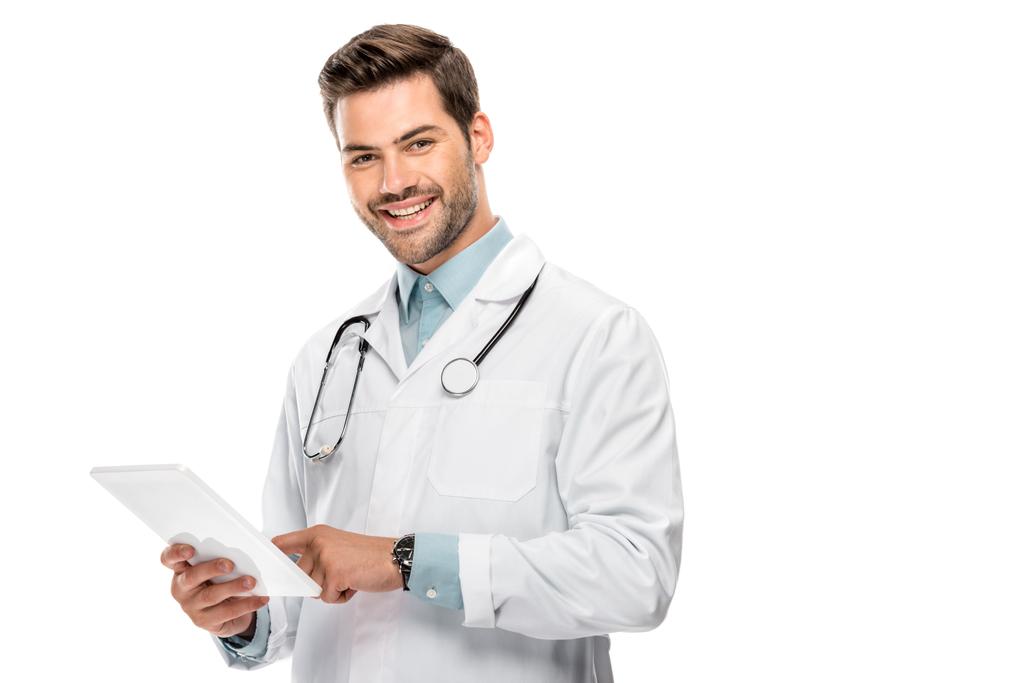 giovane medico sorridente in cappotto medico utilizzando tablet digitale isolato su bianco
  - Foto, immagini