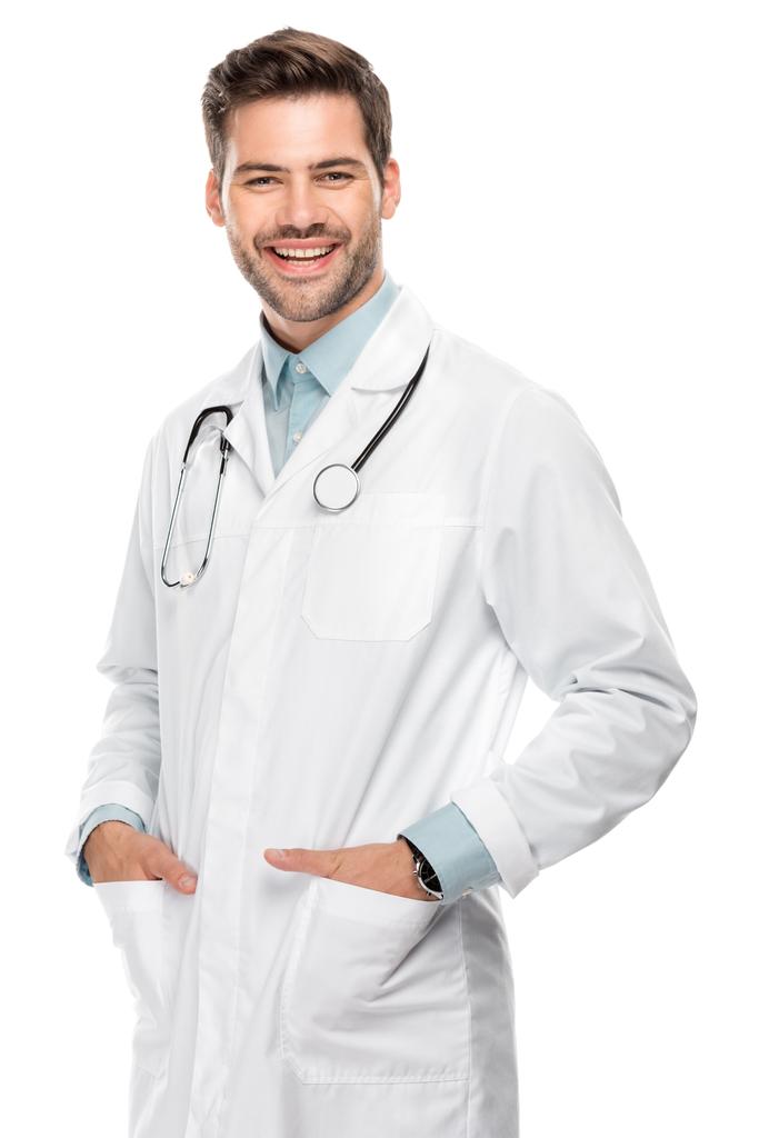 uśmiechnięty młody lekarz z stetoskop szyję w płaszcz medyczny na białym tle  - Zdjęcie, obraz