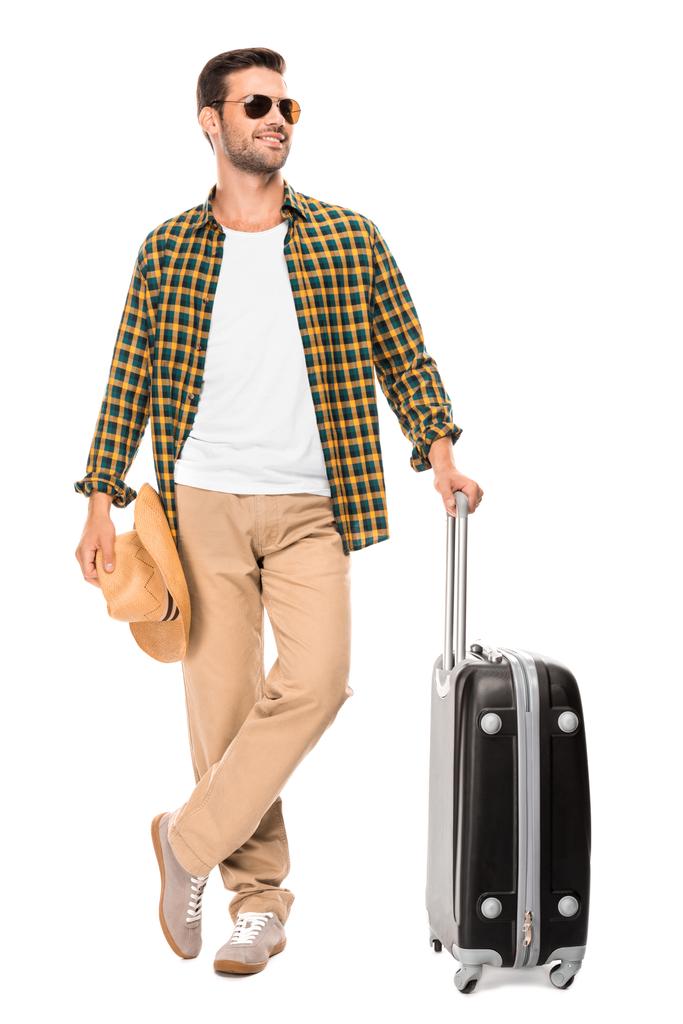 smiling young male traveler in sunglasses standing with wheeled bag isolated on white - Photo, Image