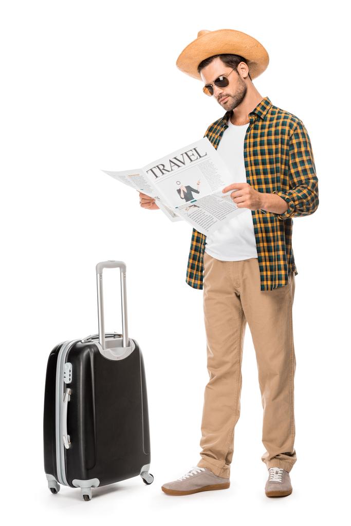 turista masculino con estilo en gafas de sol leyendo periódico de viaje cerca de la bolsa de ruedas aislado en blanco
  - Foto, imagen