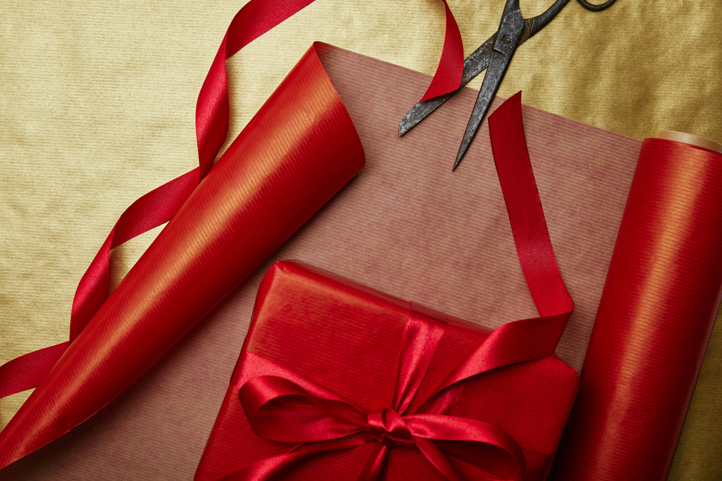 bovenaanzicht schaar en kerstcadeau met lint op rode en gouden verpakking papieren achtergrond - Foto, afbeelding
