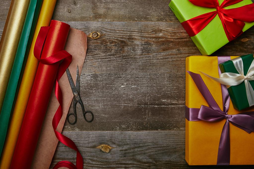 вид сверху на расположение оберточной бумаги, новогодние подарки с лентами и ножницами на деревянном столе
 - Фото, изображение