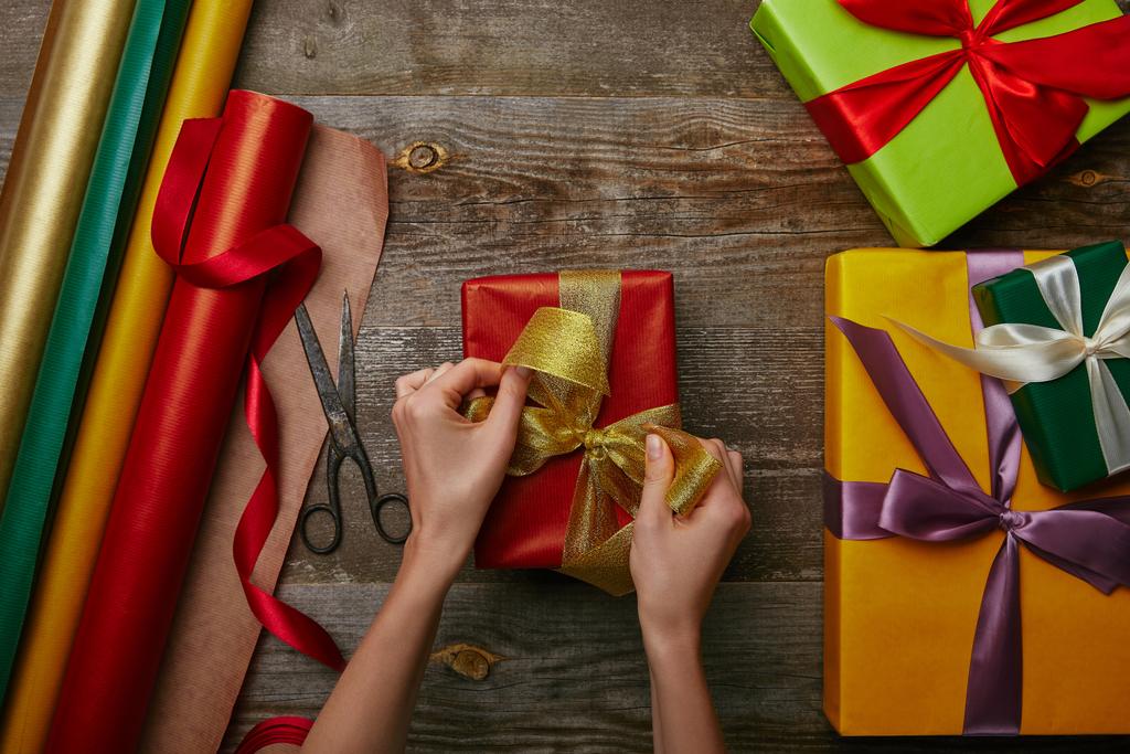 plan recadré de femme attachant ruban sur Noël enveloppé présent sur la surface en bois avec d'autres cadeaux
  - Photo, image