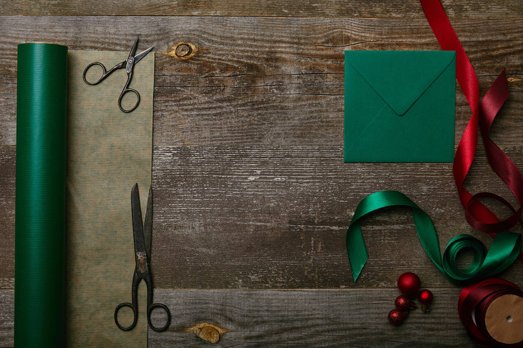 白紙の封筒、はさみ、緑と赤のリボンと木製の表面は、クリスマスの背景に包装紙とフラット レイアウト - 写真・画像