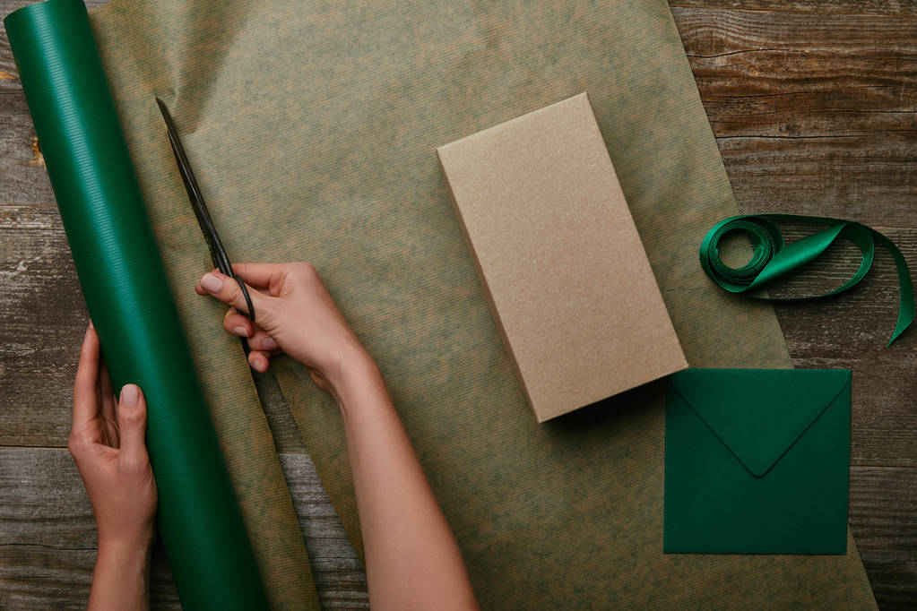 vista parziale della donna che taglia carta da regalo con forbici su superficie di legno con regalo e busta
 - Foto, immagini