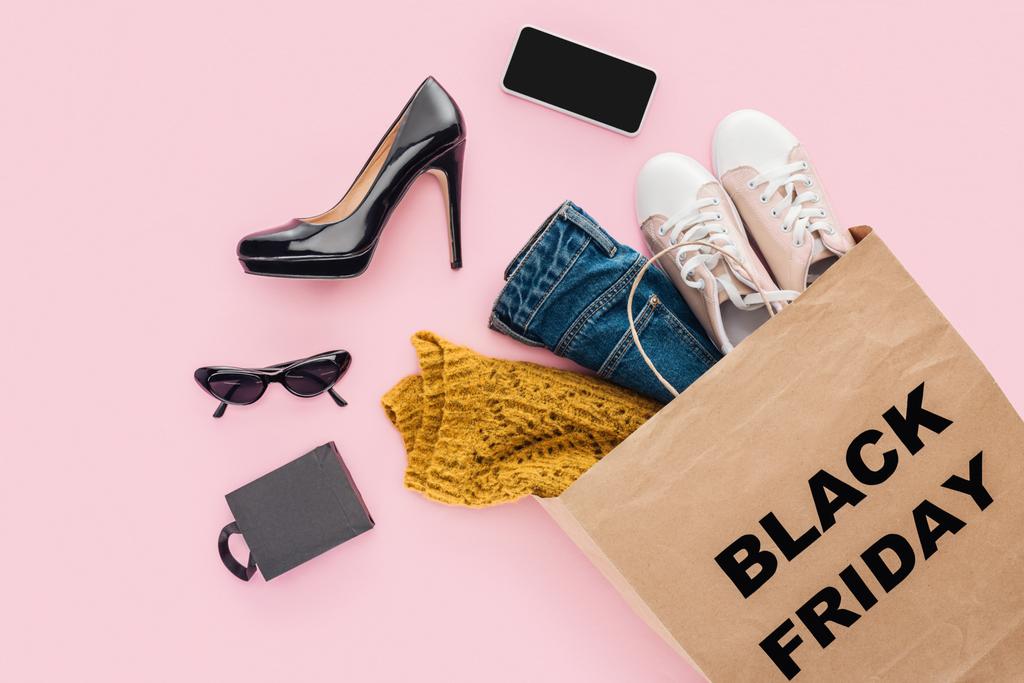 flat lay with clothes in shopping bag with black friday sign isolated on pink - Photo, Image