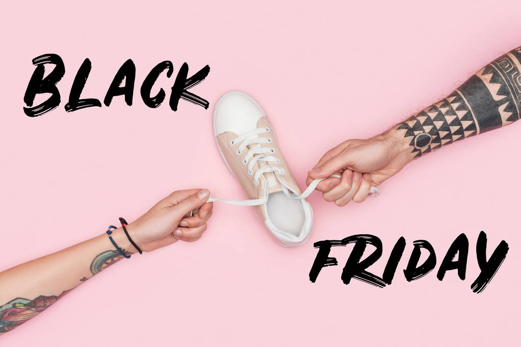vista recortada de clientes tatuados tirando de cordones de zapatillas aisladas en rosa con signo de viernes negro
  - Foto, Imagen