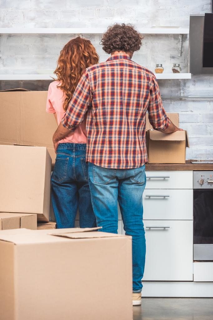 back view of couple hugging and unpacking cardboard box in new kitchen - Photo, Image