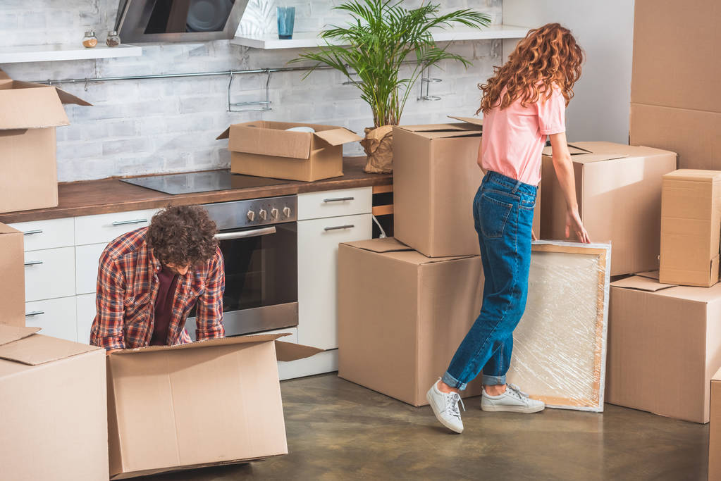 пара з кучерявим волоссям розпаковує картонні коробки в новому будинку
 - Фото, зображення