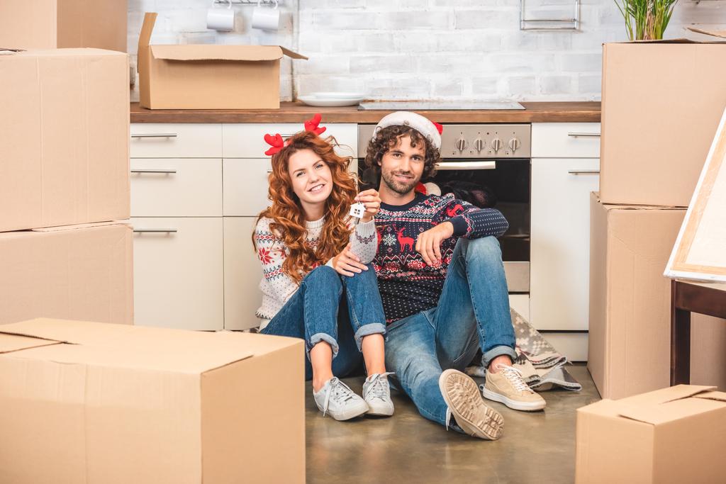 happy young couple holding keys and smiling at camera while sitting in new apartment at christmastime - Photo, Image