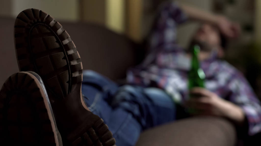 Зависимый человек в обуви спит на диване с бутылкой пива в руке, расслабиться
 - Фото, изображение