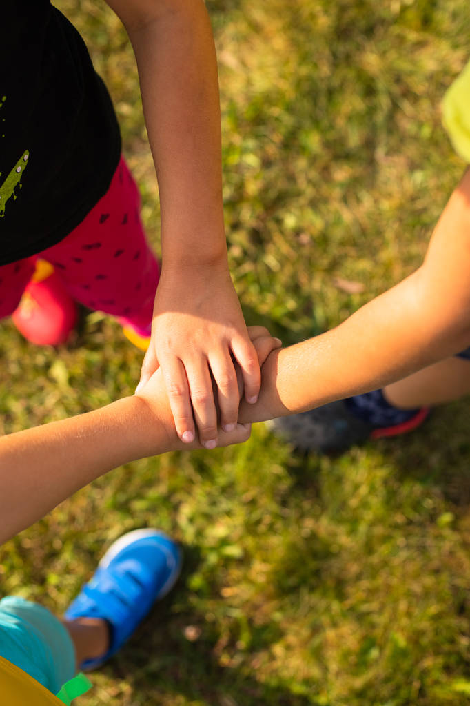 Groep van drie actieve kinderen handen samen deelnemen aan gezamenlijke spel buiten In Park In zomer bovenaanzicht. - Foto, afbeelding
