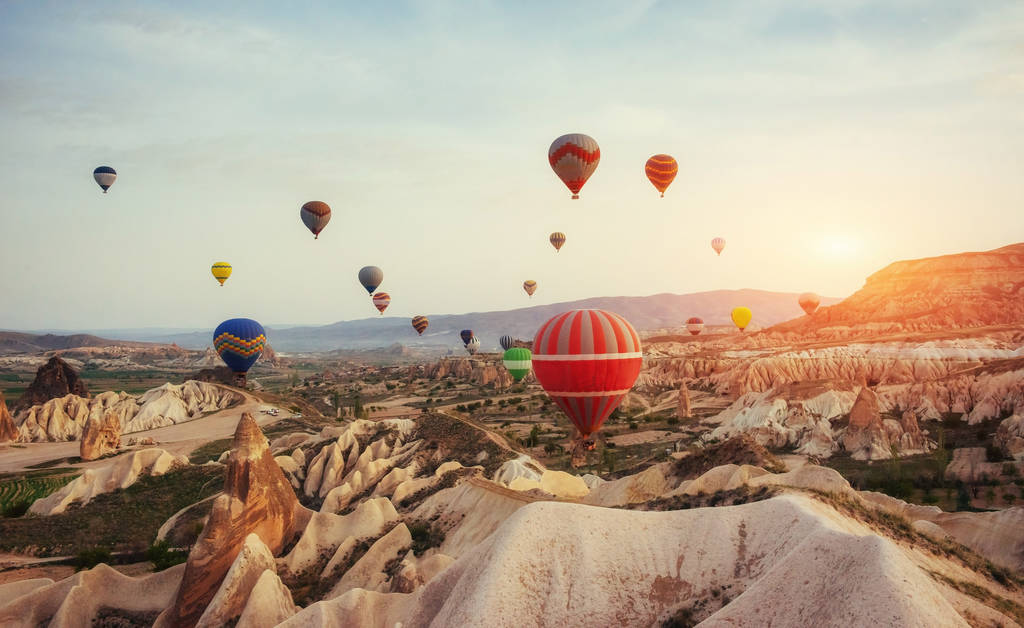 Πολύχρωμα αερόστατα που πετούν πάνω από την κόκκινη κοιλάδα στην Καππαδοκία, Ανατολίας στην Τουρκία. Ηφαιστειακά βουνά στο εθνικό πάρκο του Γκιόρεμε. - Φωτογραφία, εικόνα