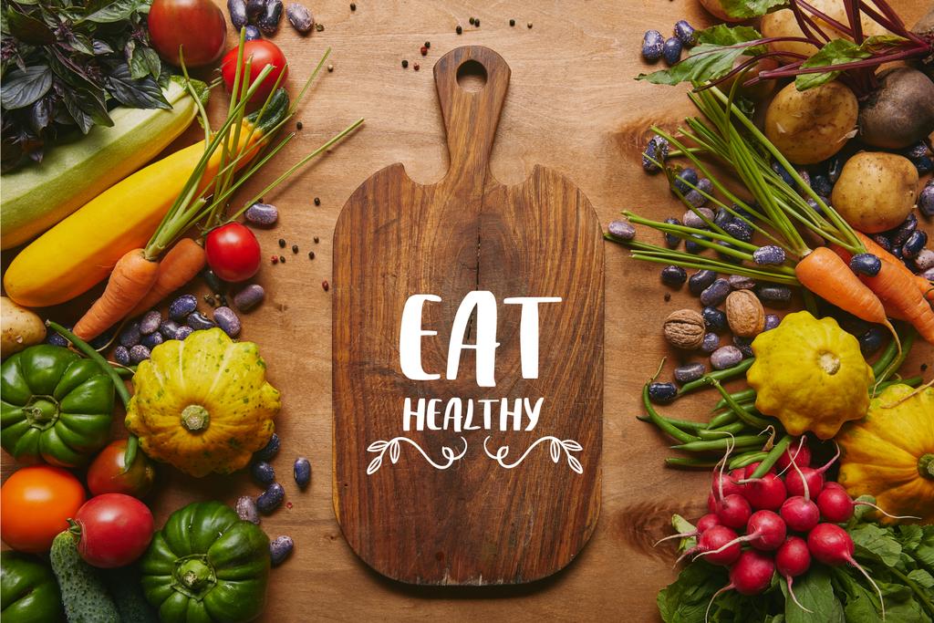 Cutting board with "eat healthy" lettering and summer vegetables on wooden table - Photo, Image