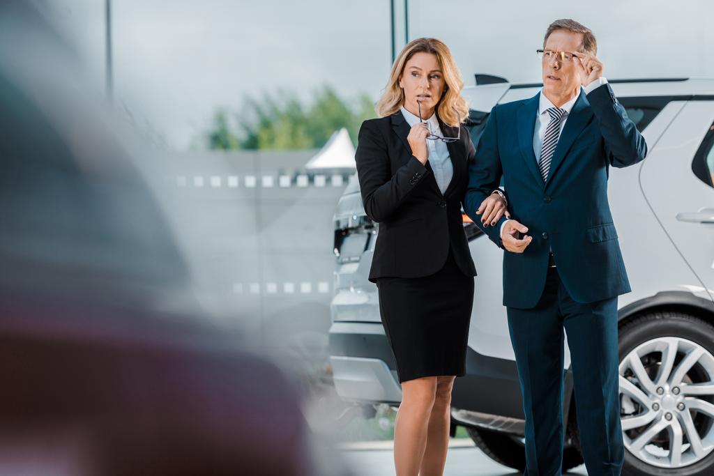 задумчивый бизнесмен и деловая женщина выбирают новый автомобиль в выставочном зале
 - Фото, изображение