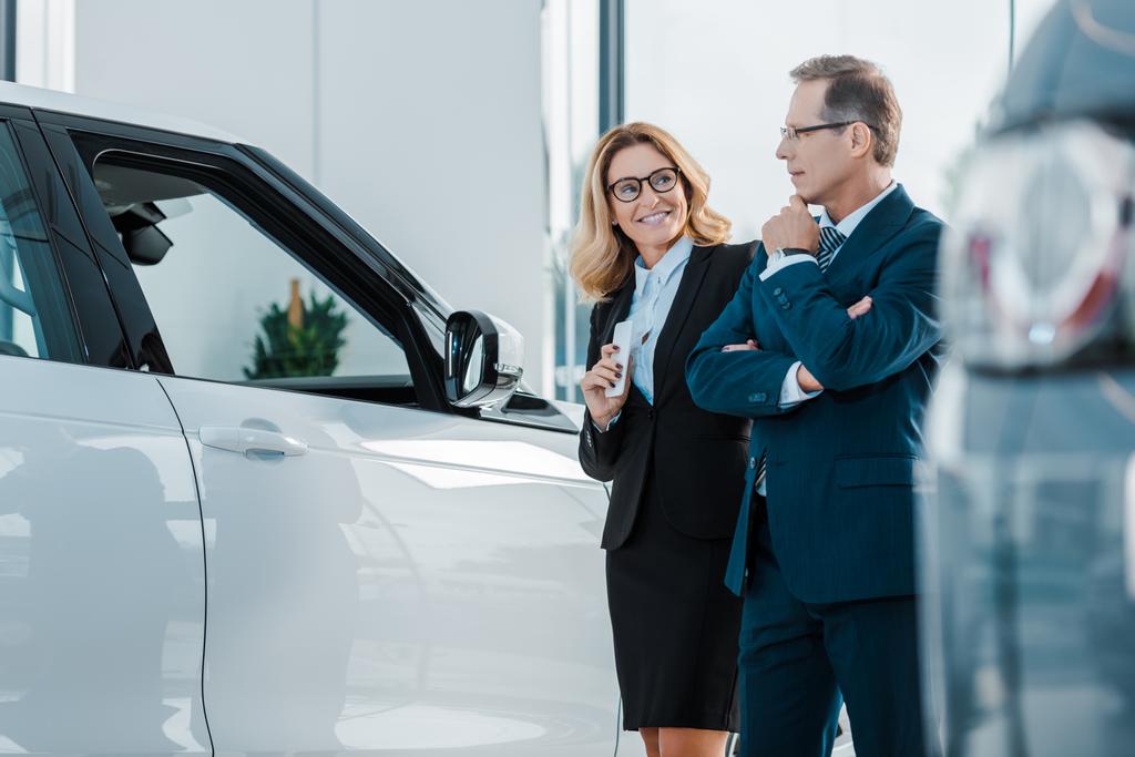 sonriente pareja de negocios en busca de un nuevo automóvil en el salón de concesionarios
 - Foto, imagen