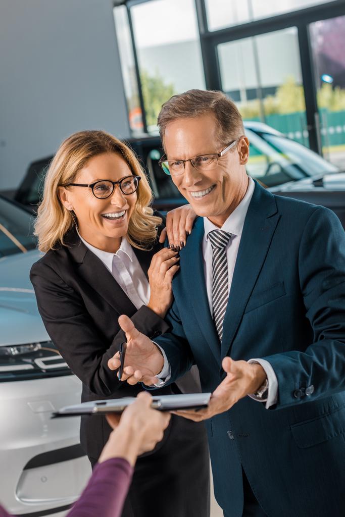feliz pareja de negocios firmando papeles para comprar un coche nuevo en la sala de exposición
 - Foto, imagen
