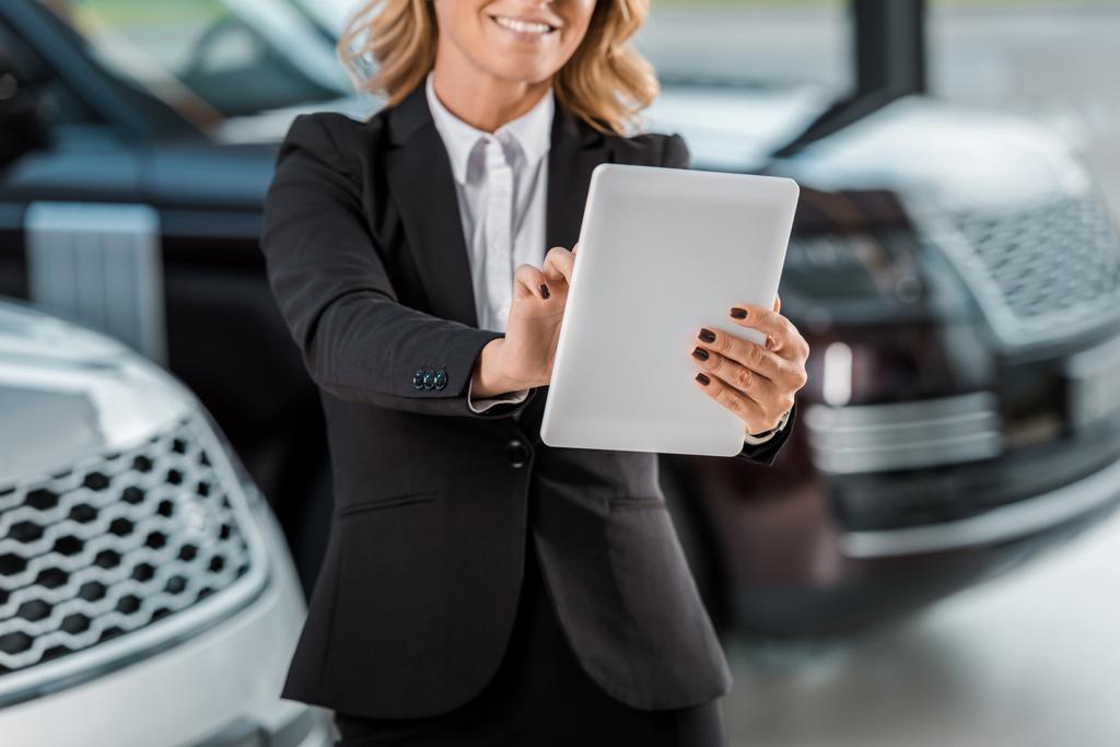 bijgesneden schot van glimlachen vrouwelijke autohandelaar holding tablet in showroom - Foto, afbeelding