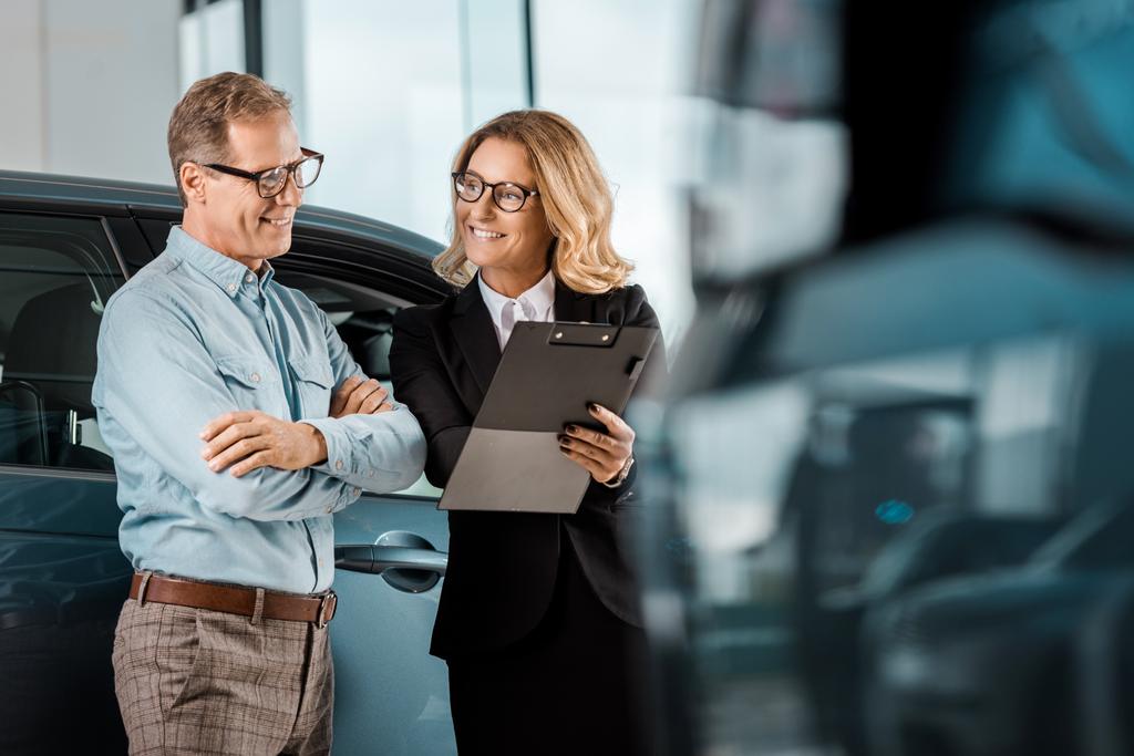adult man and female car dealer with clipboard standing at showroom - Photo, Image