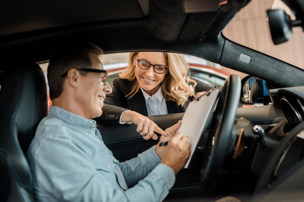 dospělý muž podepsání smlouvy s ženské autoprodejce zatímco sedí v autě - Fotografie, Obrázek
