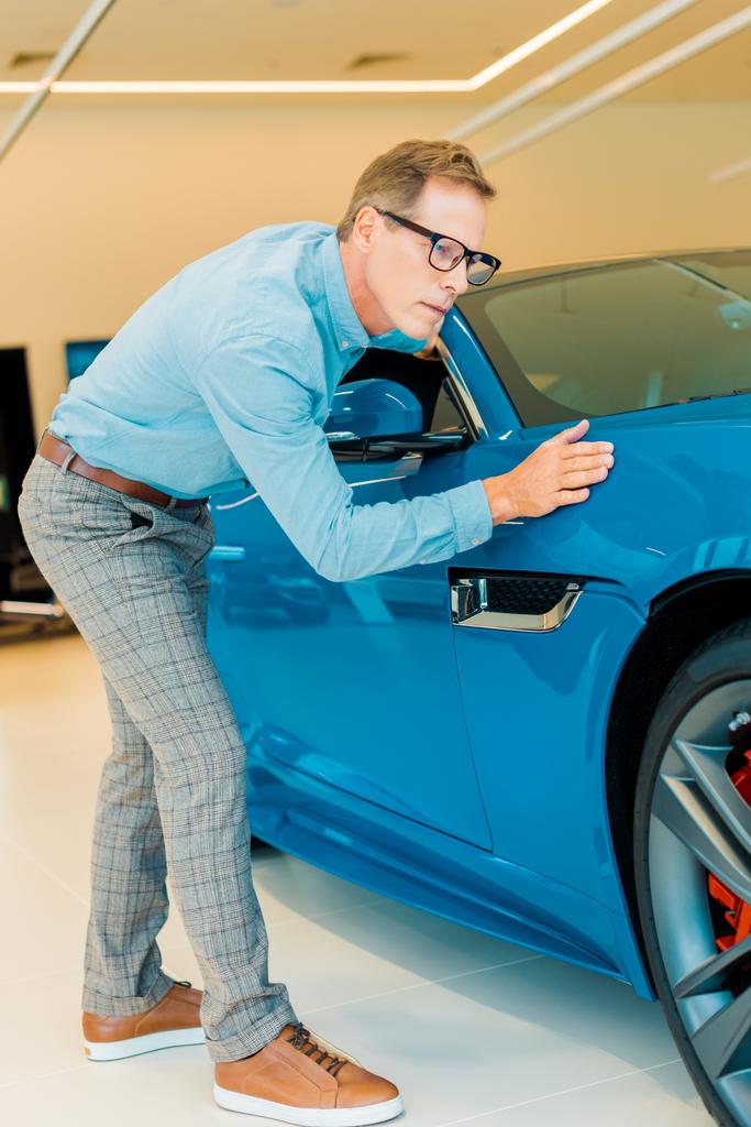 attractive adult man touching luxury sport car at showroom - Photo, Image