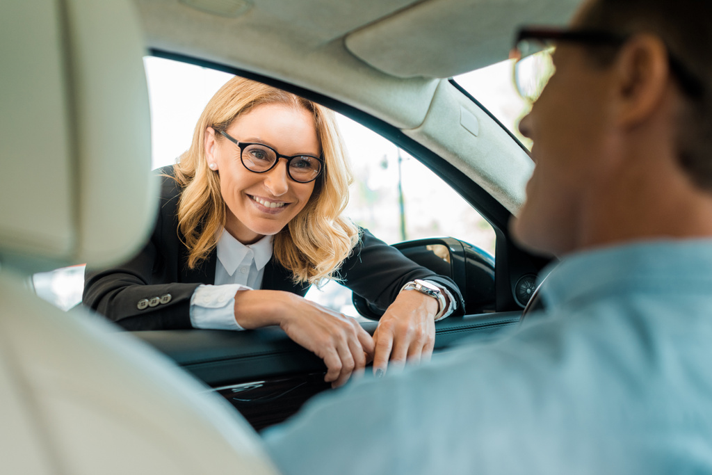 hombre adulto hablando con concesionario de coche femenino mientras está sentado dentro del coche en la sala de exposición
 - Foto, Imagen