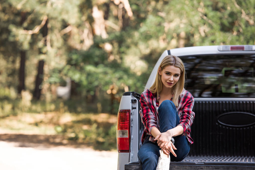 ευτυχής όμορφη κοπέλα βλέπουν φωτογραφική μηχανή και να κάθεται σε φορτηγό επαναλείψεων στο δάσος - Φωτογραφία, εικόνα