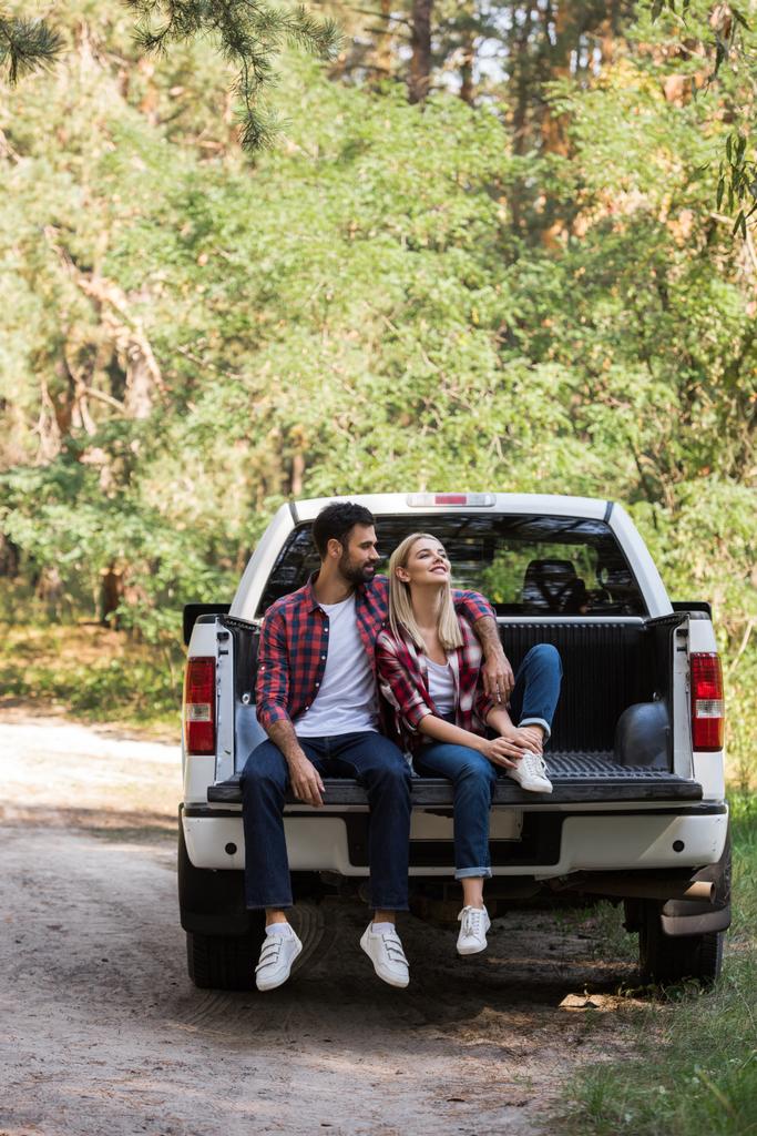 couple hugging and sitting together on pickup truck in forest - Photo, Image