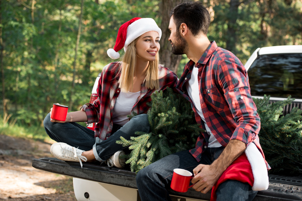 attraktive Frau mit Freund, während sie im Kofferraum mit Weihnachtsbaum im Freien sitzt  - Foto, Bild