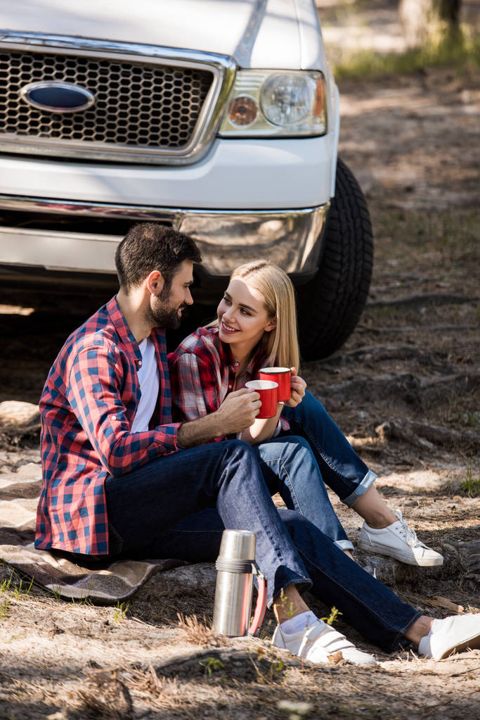 sorridente coppia avendo pic-nic con bevanda calda sulla coperta vicino pick-up camion
  - Foto, immagini