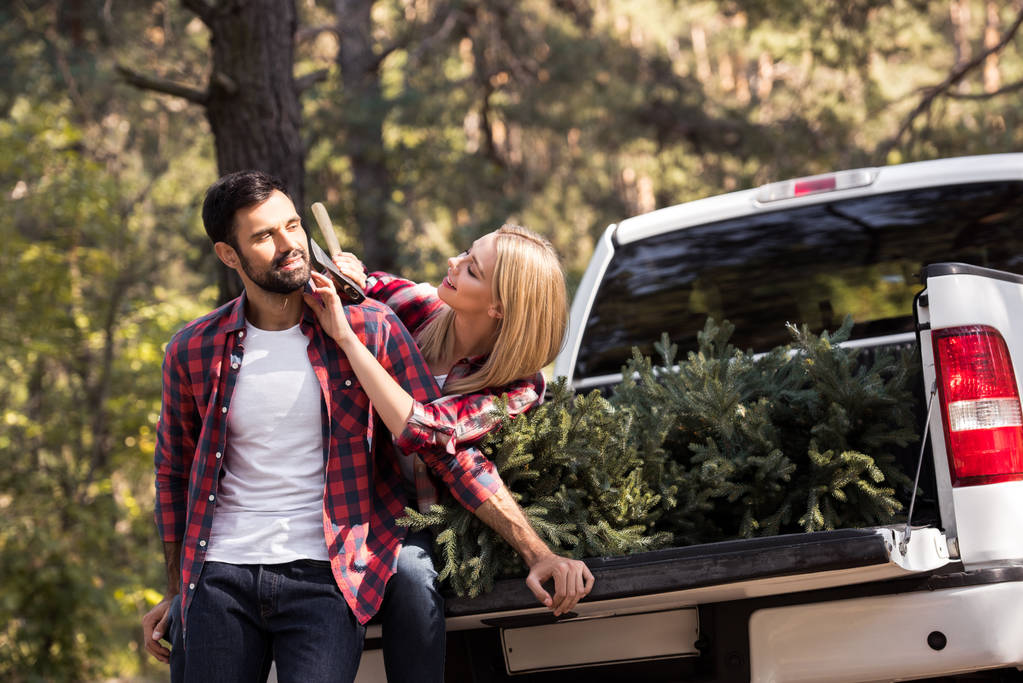 Namorada tentando barbear namorado com machado enquanto sentado na pickup caminhão com abeto para o natal na floresta
 - Foto, Imagem