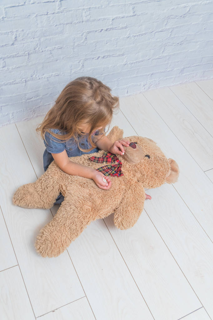 la ragazza, bambino tratta un orso giocattolo, una pillola di fronte a un muro di mattoni bianchi
 - Foto, immagini