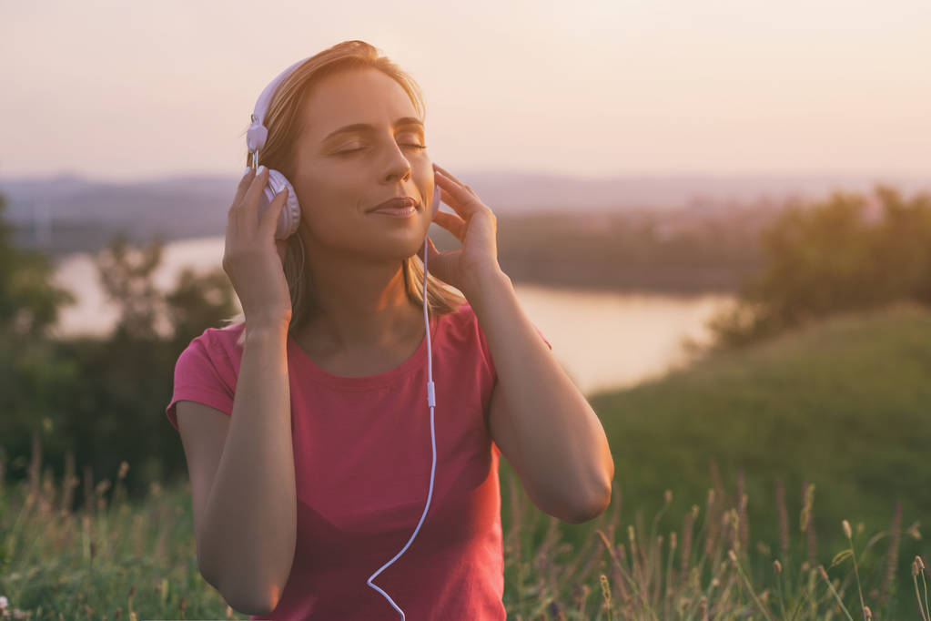 Mulher bonita gosta de ouvir música ao ar livre com uma paisagem urbana e vista para o rio atrás dela.A imagem é intencionalmente tonificada
. - Foto, Imagem