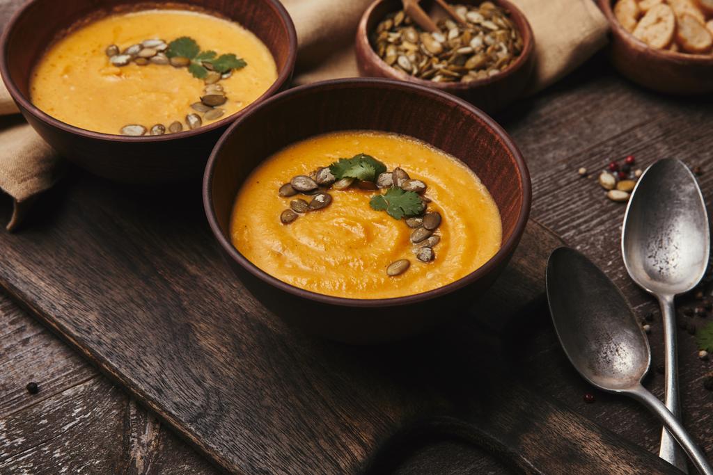 close-up view of bowls with organic pumpkin soup on wooden cutting board - Photo, Image